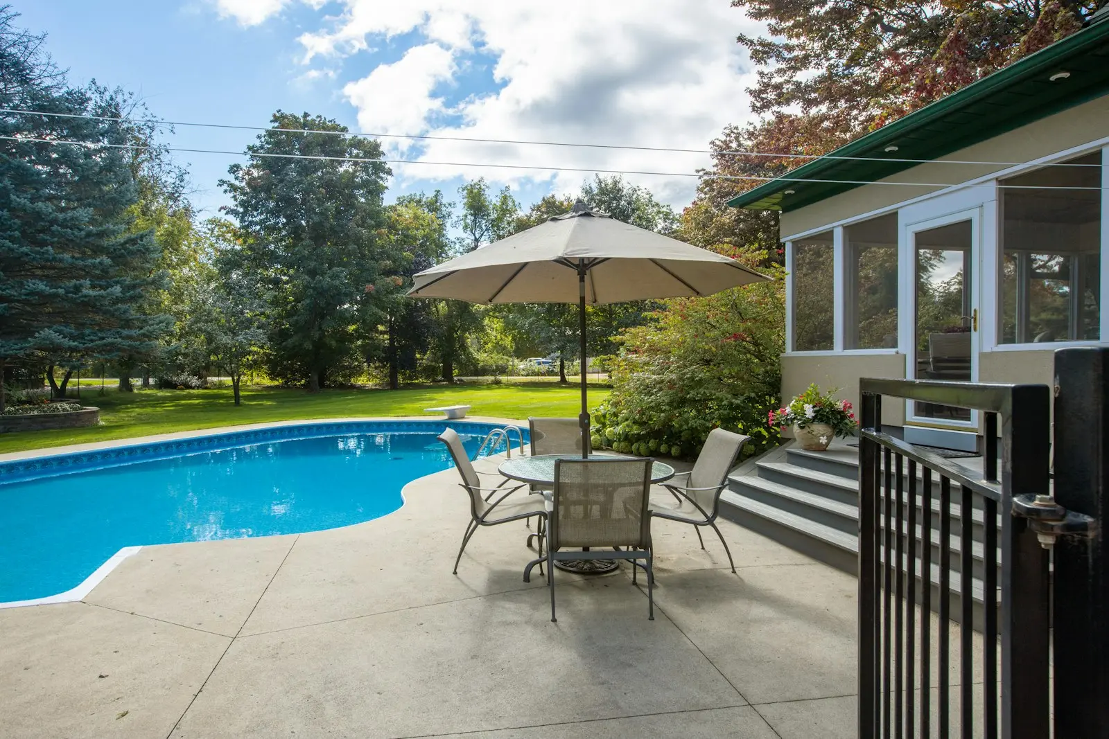 Terrasse de jardin avec table et parasol au bord d'une piscine, fermée par une barrière